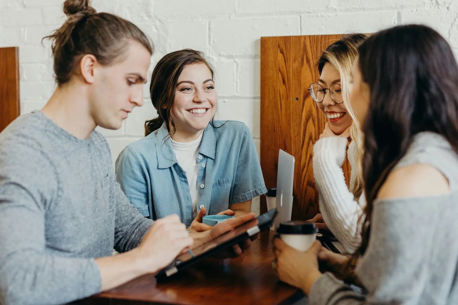Four university students laughing around a table with a tablet and a laptop